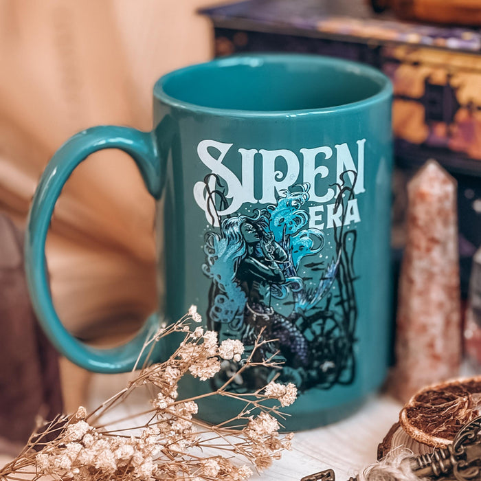 A blue mug with a mermaid pictured on it and the text Siren Era in white decorative font